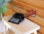 1:12 scale miniature classic typewriter in black with white keys, shown on a light wood desk