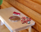 1:10 scale miniature red stapler, shown on a wood desk beside a coin for scale