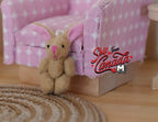 1:12 scale miniature plush bunny doll in beige with jointed limbs and long ears, sitting against a pink gingham sofa