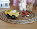 1:12 scale miniature yellow toy pickup truck with black wheels, shown on a round woven rug near plush toys