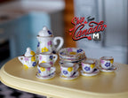 1:12 scale miniature porcelain tea set with multicolor leaf pattern, set of 15, shown on a yellow table