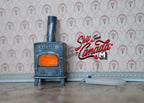 1:12 scale miniature wood burning stove fireplace in blue gray with a glowing orange LED fire light and a chimney pipe