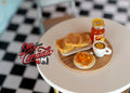 1:12 scale miniature breakfast plate with jam toast, jam jar and cup on a round wood board, shown on a white table