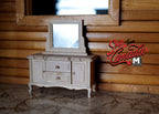 1:12 scale miniature dresser with mirror, swing door and 2 drawers in bare wood, shown against a log cabin wall