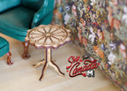 1:12 scale miniature light brown wood pie crust tripod table with round scalloped top, shown beside a green armchair
