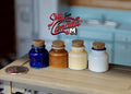 1:12 scale miniature kitchen canisters with cork lids in navy, brown, cream and white, set of 4, on a wood counter