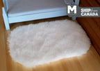 1:12 scale miniature faux sheepskin rug in white, fluffy long pile, shown on a wood floor beside a blue bed
