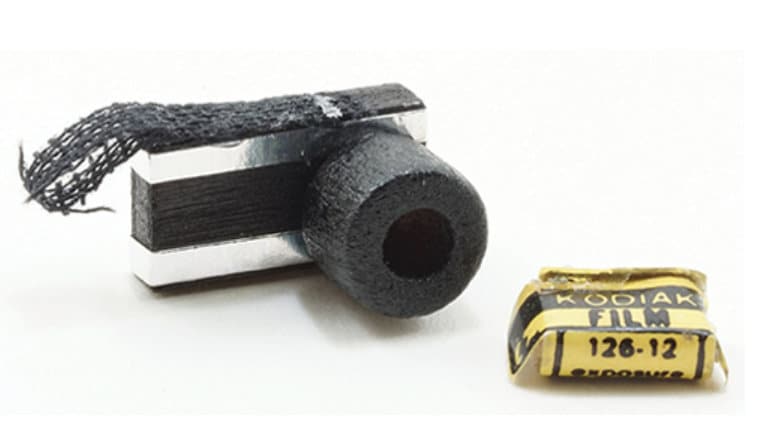 1:12 scale miniature old style camera in black and silver with strap and yellow film box, on a white background