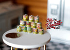 1:12 scale miniature metal vegetable and fruit tin cans with printed labels, set of 12, stacked on a white table by a coin