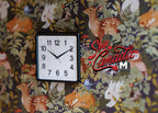 1:12 scale miniature square wall clock in black and white with printed numbers, non working, on floral wallpaper