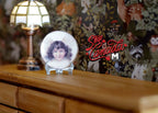 1:12 scale miniature ceramic wall plate with angel design on a metal stand, shown on a wood dresser beside a lit lamp