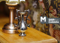 1:12 scale miniature metal urn vase in silver with scroll handles on a pedestal, on a wood table beside a lamp