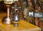1:12 scale miniature metal urn vase in silver with scroll handles on a pedestal, on a wood table beside a lamp