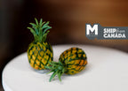 1:12 scale miniature pineapples, set of 2, yellow and green with leafy crowns, shown on a white round table