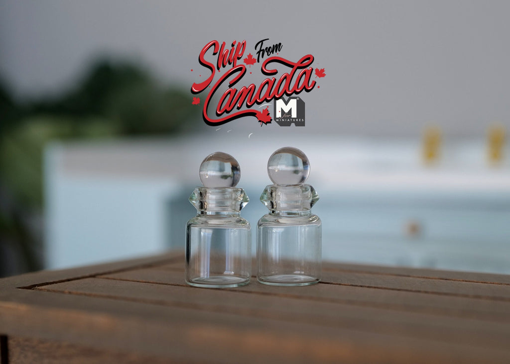 1:12 scale miniature clear glass bottles with ball stoppers, set of 2, shown on a dark wood table