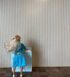 1:12 scale miniature pinstripe wallpaper in multicolor pastel vertical stripes, shown on a wall behind a doll