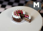 1:12 scale miniature sliced strawberry chocolate layer cake with cream border and one cut slice, on a white table