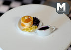 1:12 scale miniature pancake stack with blueberries, banana and berry jam on a white plate, with a sauce boat of jam