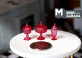 1:12 scale miniature footed candy dishes with lids in clear red, set of 3 shapes, on a white round table beside a coin