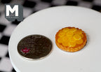 1:12 scale miniature orange pie with glazed orange slices in a golden crust, on a white table beside a coin for scale