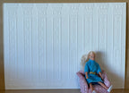1:12 scale miniature ornate pilaster wall panel in white embossed foam board, shown behind a seated figure in an armchair