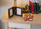 1:12 scale miniature metal double folding photo frame in dark bronze tone, shown open on a desk beside books