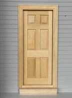 1:12 scale miniature unfinished classic 6 panel interior wood door with back trim, shown set in a gray sided wall