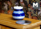 1:12 scale miniature ceramic flower pot, white with blue stripes and ruffled rim, shown on a wood shelf by a coin