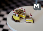 1:12 scale miniature cherry and chocolate cake with cream rosettes and a slice cut out, shown on a round white table