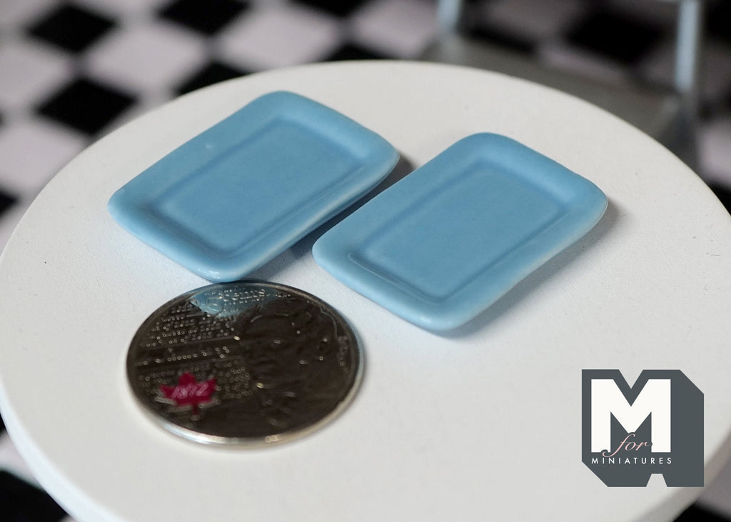 1:12 scale miniature light blue rectangular plates with rounded corners, set of 2, shown on a white table beside a coin