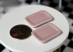 1:12 scale miniature ceramic rectangle plates in pink with raised rims, set of 2, shown beside a coin for scale