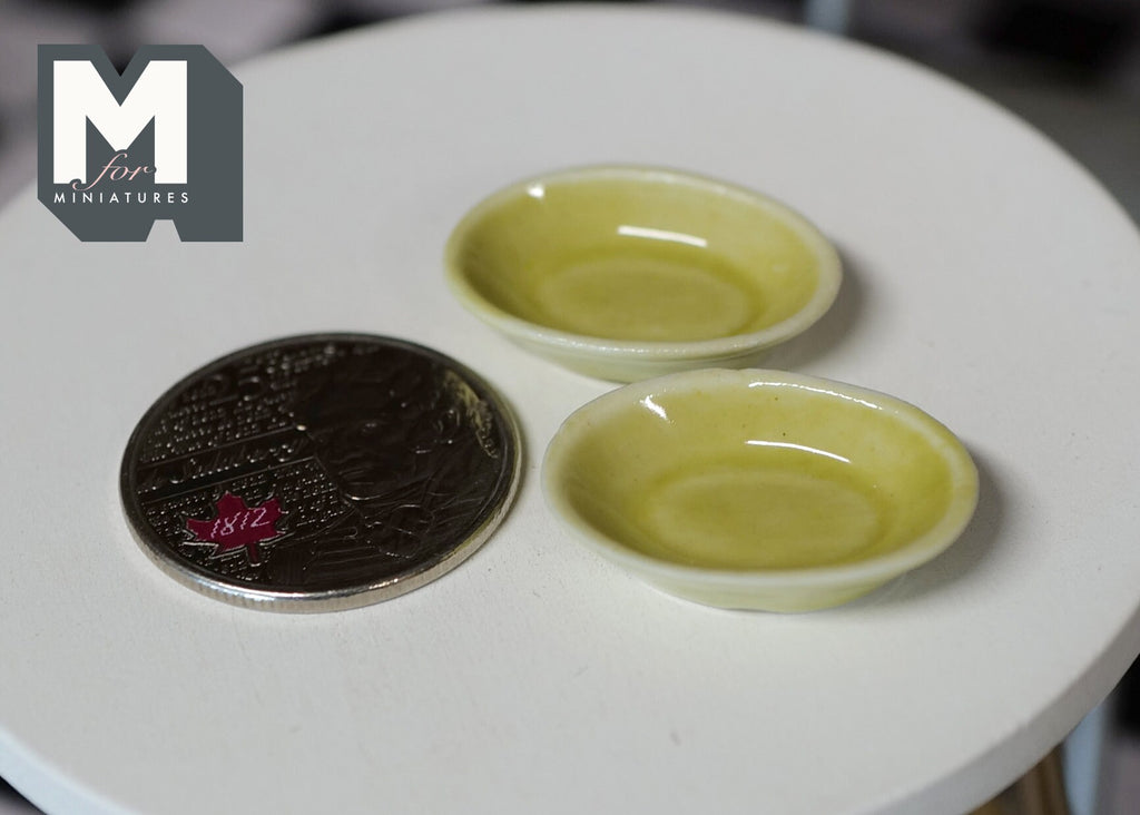 1:12 scale miniature ceramic plates in olive green glaze, set of 2, on a round white table beside a coin for scale