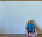 1:12 scale miniature Ionic column wall panel in white embossed foam board, shown behind a seated figure in an armchair