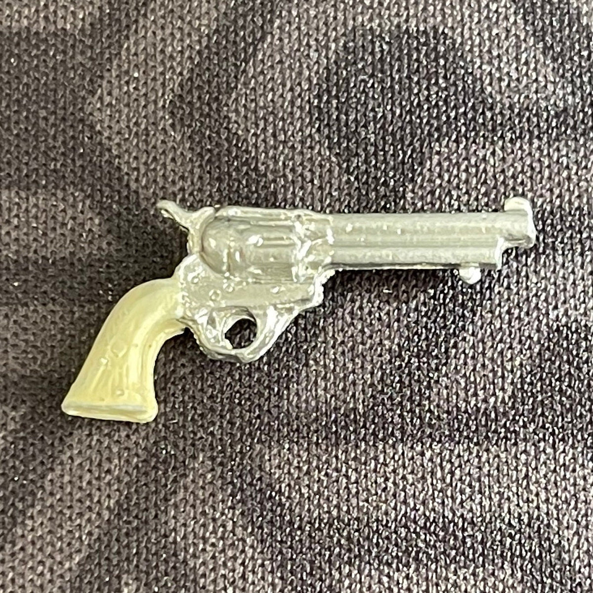 1:12 scale miniature western revolver with cream grip and silver long barrel, non working, on gray fabric