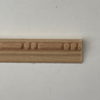 Miniature bead and reel wood trim molding for walls, unfinished wood with carved bead detail, close-up on a white surface