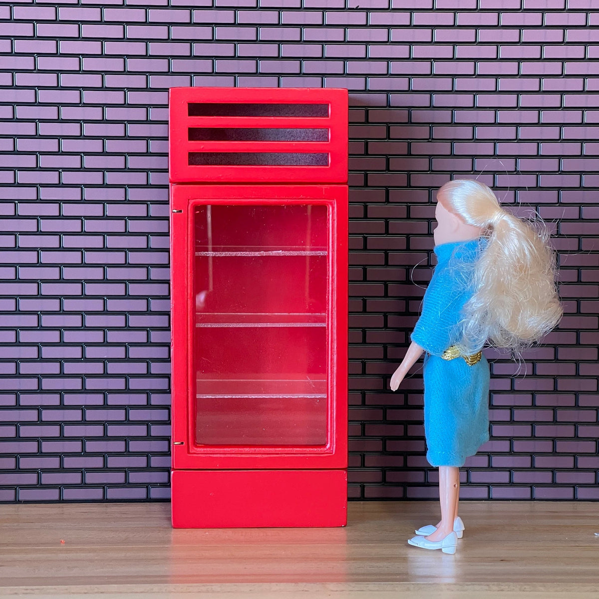 1:12 scale miniature red beverage cooler with glass door and 4 clear shelves, shown beside a doll for scale