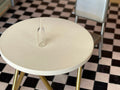 1:12 scale miniature clear glass water bottle with narrow neck, shown on a round cream table over a checkered floor