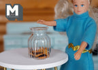 1:12 scale miniature glass cookie jar with chocolate cookies, ribbed clear jar shown on a white table beside a doll