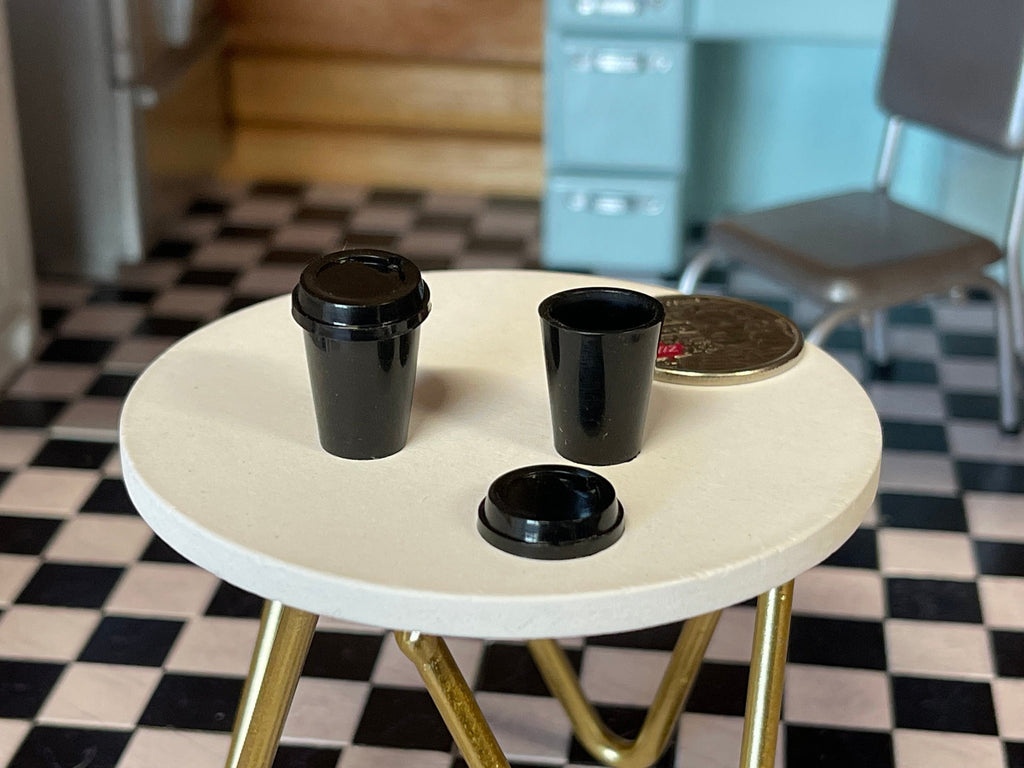 1:6 scale miniature black coffee cups with lids, set of 2, takeout style, shown on a white table with a coin