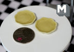 1:12 scale miniature ceramic plates with rim in yellow, set of 2, on a round white table beside a coin for scale