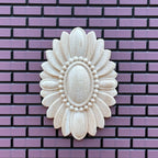 1:12 scale miniature unfinished oval floral ceiling rose with beaded center, small, cream, shown on a purple brick wall