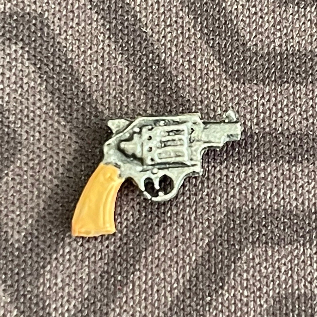 1:12 scale miniature snub nose revolver with tan grip and silver body, non working, shown on gray fabric