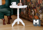 1:12 scale miniature white wood round pedestal end table with tripod base, shown beside a green armchair