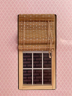 1:12 scale miniature bamboo roll up window shade in natural tan, fixed, shown half rolled above a wood window