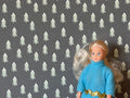 1:12 scale miniature gray snowy pine tree wallpaper with rows of small white trees, shown behind a doll for scale
