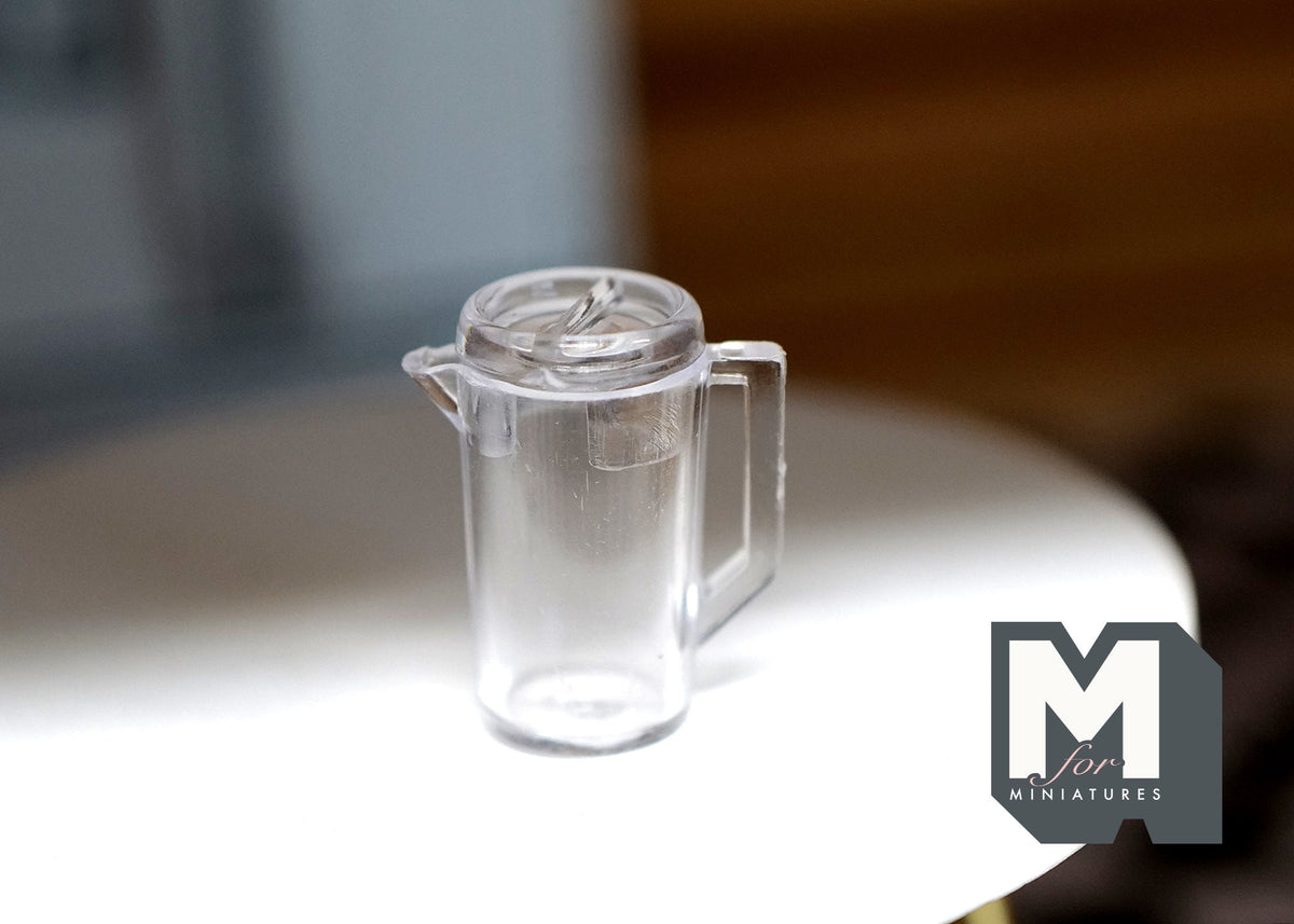 1:12 scale miniature clear water pitcher with handle and spout, shown empty on a round white table