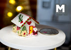 1:12 scale miniature gingerbread house in snowy white and green with a Santa by the door, shown beside a coin