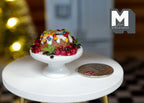 1:12 scale miniature Christmas cake on white pedestal stand with white icing, sprinkles and red berries, beside a coin