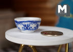 1:12 scale miniature ceramic bowl in white with blue floral pattern, shown on a white round table beside a coin