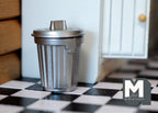 1:12 scale miniature metal garbage can in silver with lid and ribbed sides, small, on a black and white checkered floor